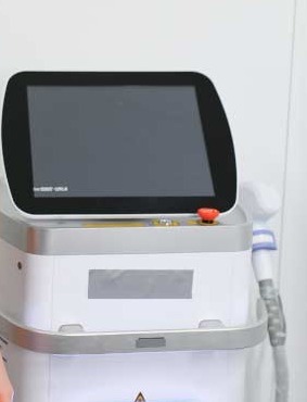 A laser treatment platform with a touchscreen console, an emergency stop and a handpiece resting in its cradle.